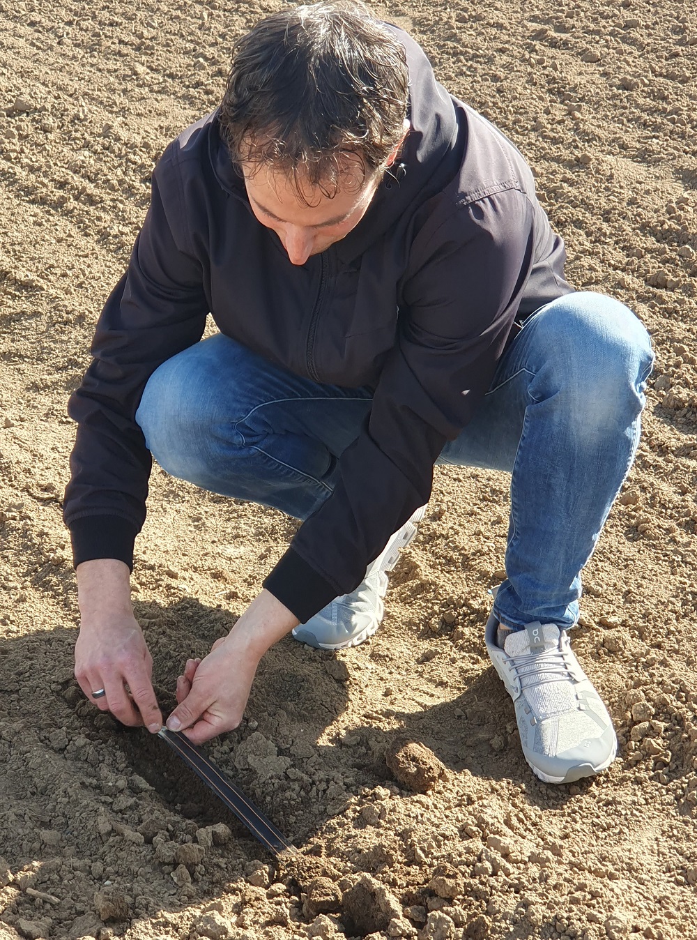 Manuel Metzger zeigt der Gruppe einen unter der Erde im Acker verlegten Bewässerungsschlauch