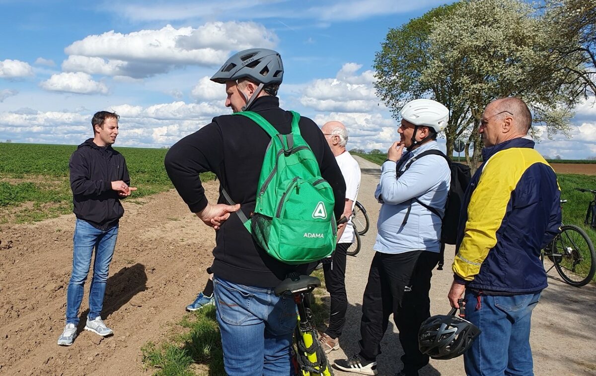 Manuel Metzger spricht mit der Radlergruppe am Rand eines Ackers.