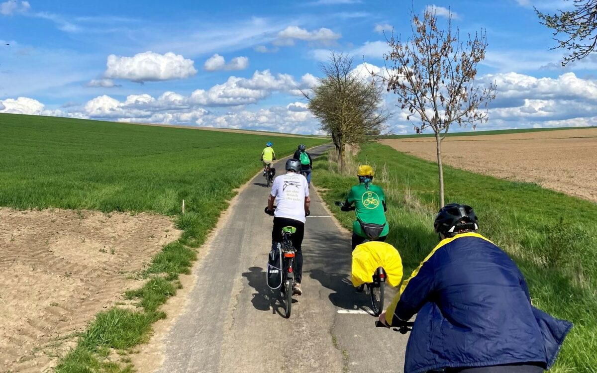 Eine Gruppe Radler fährt auf einem Flurbereinigungsweg zwischen einer Wiese und einem Acker entlang