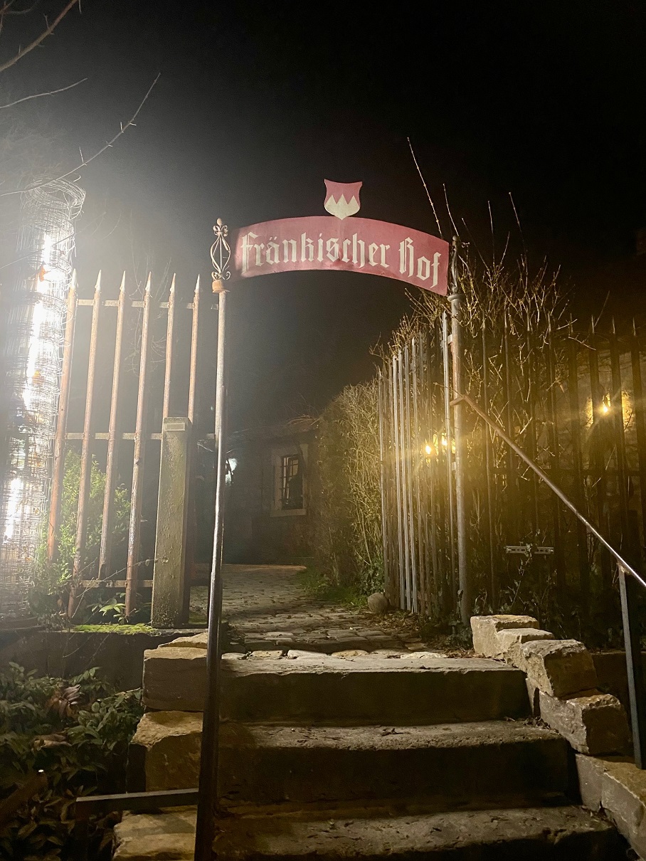 Bild vom Eingang der Wirtschaft Fränkischer Hof. Rotes Schild mit Flagge Unterfrankens darüber. 