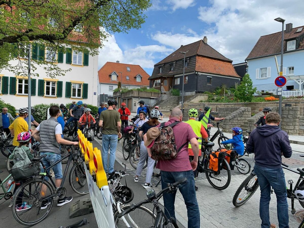 Die Fahrradgruppe auf einem zentralen Platz am Losfahren. Im Hintergrund blauer Himmel. 