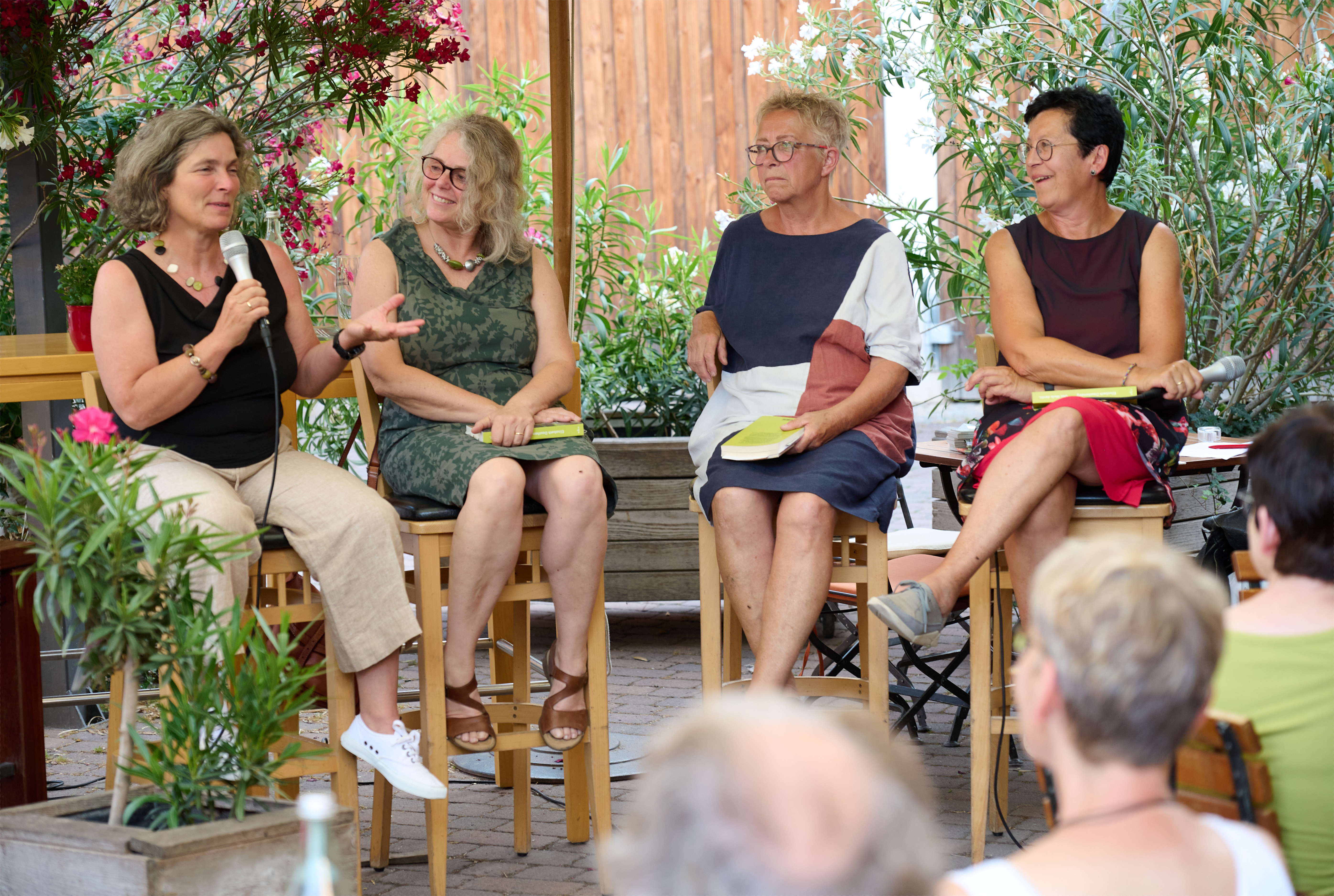 Bild von MdL Kerstin Celina, Bezirksrätin Christina Feiler, Marion Reuther, Ilse Gebhardt-Gögercin, gemeinsam auf Stühle sitzend, mit Büchern in der Hand. Kerstin Celina hat ein Mikrofon in der Hand, die anderen drei Frauen hören ihr gespannt zu.