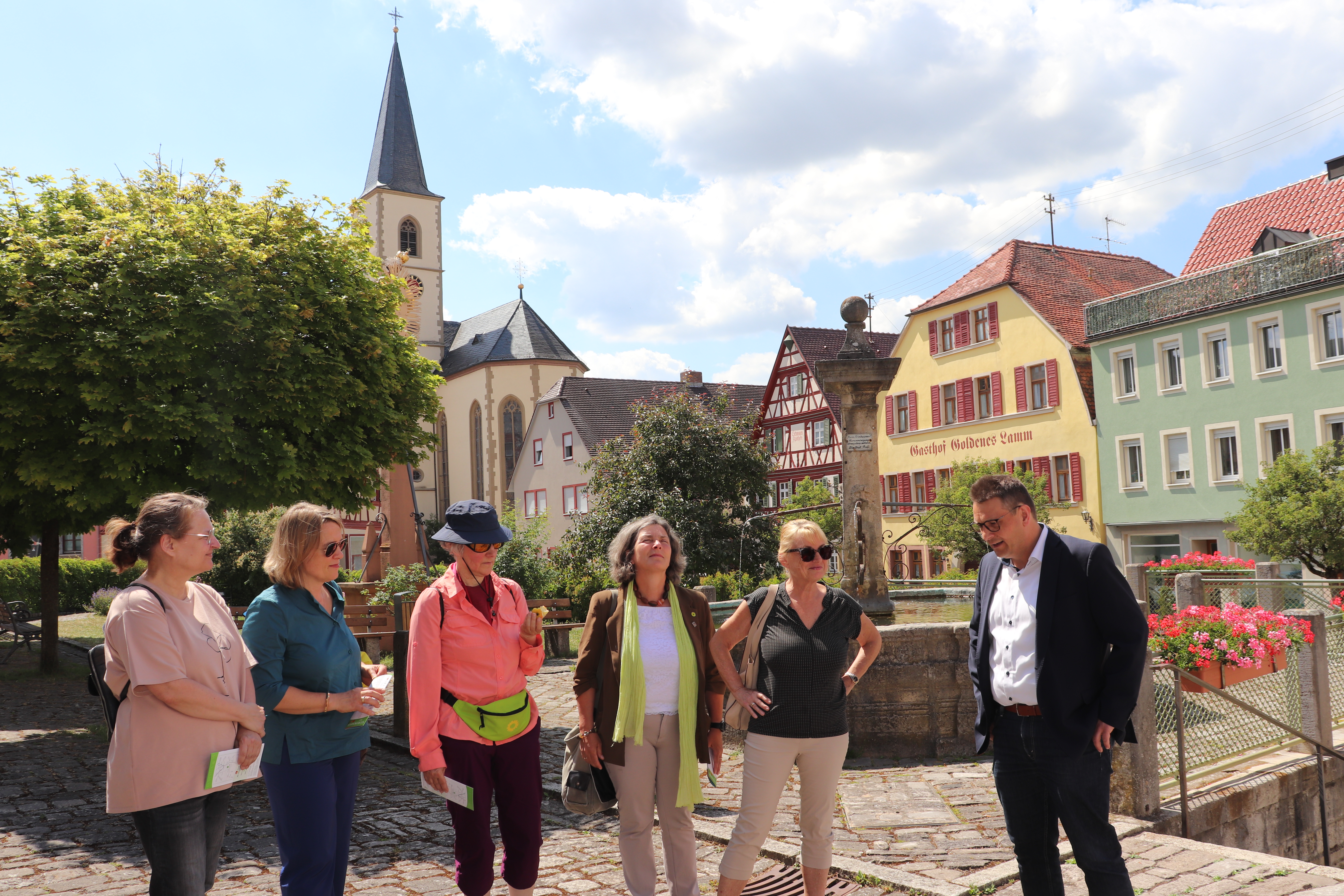Foto der Gruppe rund um die zwei MdLs Kerstin Celina und Sabine Weigand im historischen Stadtkern in Aub. Die Delegation hört zu was der Bürgermeister zu sagen hat.