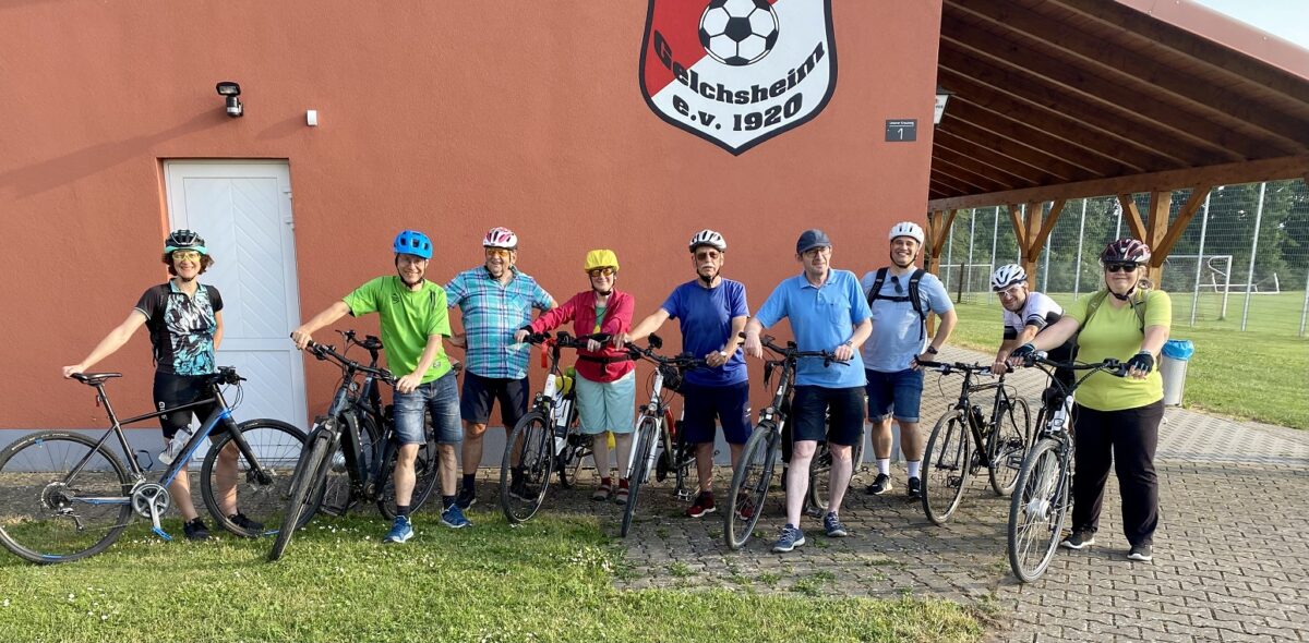 Gruppenfoto der Radfahrer/innen vor einer Pastell-rot gestrichenen Wand unter dem Vereinslogo Gelchsheim e.v. 1920. 