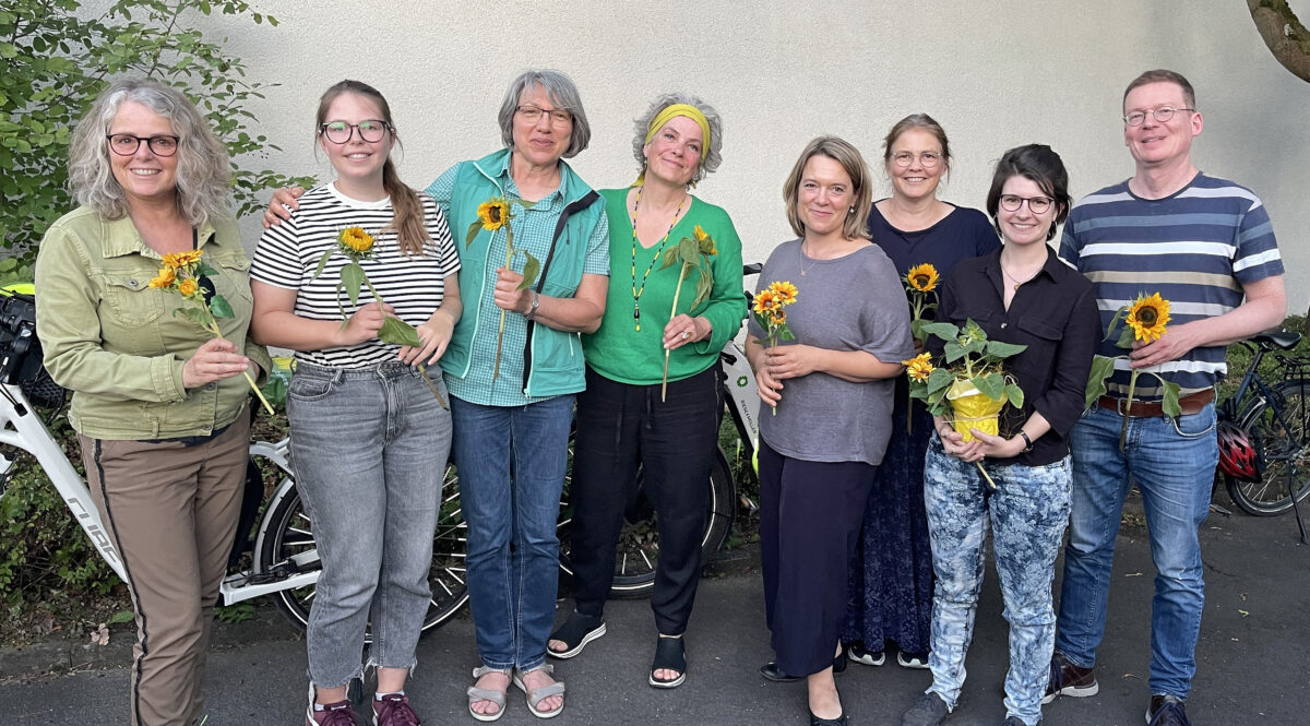 Der neu gewählte fünfköpfige Vorstand sowie Christina Feiler, Helena Kontny und Jessica Hecht stehen in einer Reihe mit Sonnenblumen in den Händen und lächeln in die Kamera. 