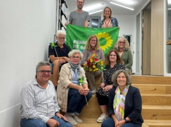 Bild auf einer Treppe. Mit Banner der Grünen in den Händen und einer Sonnenblume sitzt der neu gewählte Vorstand und Kerstin Celina, Gerhard, Müller, Christina Feiler, Sven Winzenhörlein und Jessica Hecht