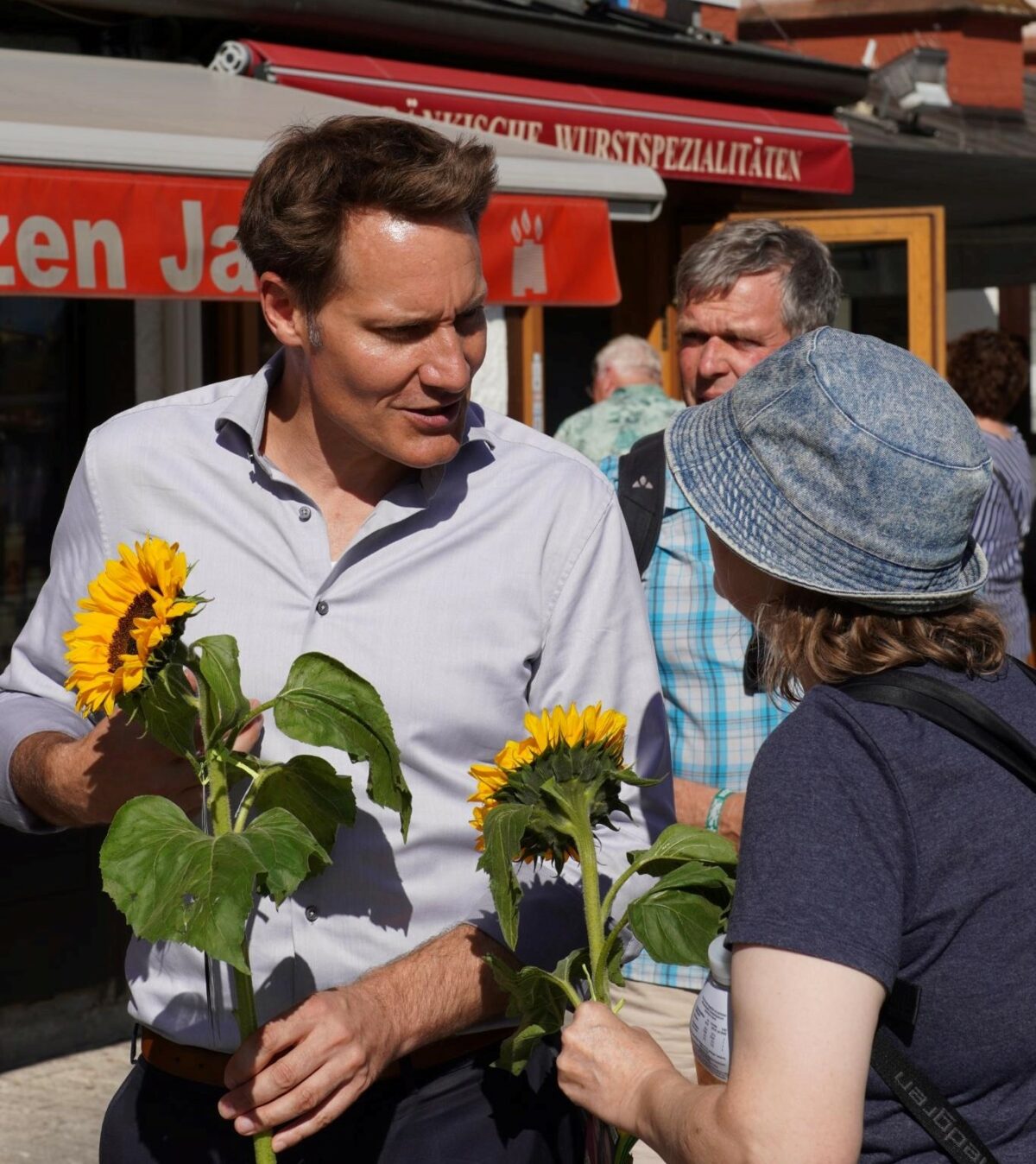 Ein Bild von Ludwig Hartmann mit einer Sonnenblume in der Hand, wie er mit einer Frau redet