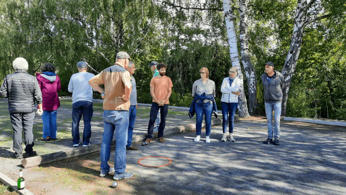 Boulerspieler*innen um das Spielfeld herum. Am Rand stehen Bäume.