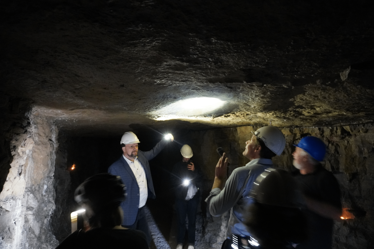 Ein Foto aus dem Stollen heraus. Eine Gruppe Menschen schaut sich den Stollen an.  Zu sehen ist Patrick Friedl. 