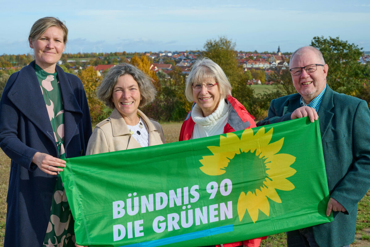 Der neugewählte GRÜNE Vorstand aus Kürnach gemeinsam mit einem Banner in der Hand stehen auf einer Wiese mit Kürnach im Hintergrund.