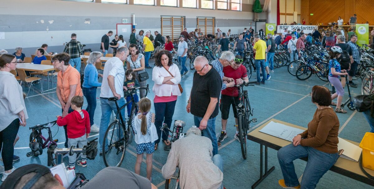 Besucherinnen und Besucher des Fahradflohmarktes gehen zwischen den Fahrrädern in der Halle umher und begutachen die Räder.